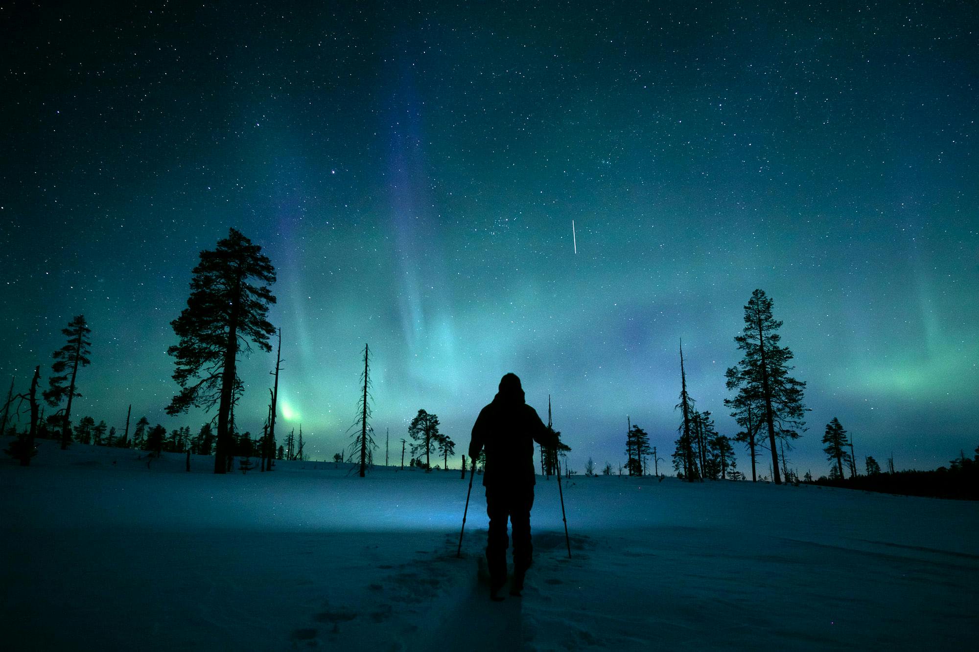Revontuliretki lumikengillä pimeässä Levin lumisessa maisemassa.