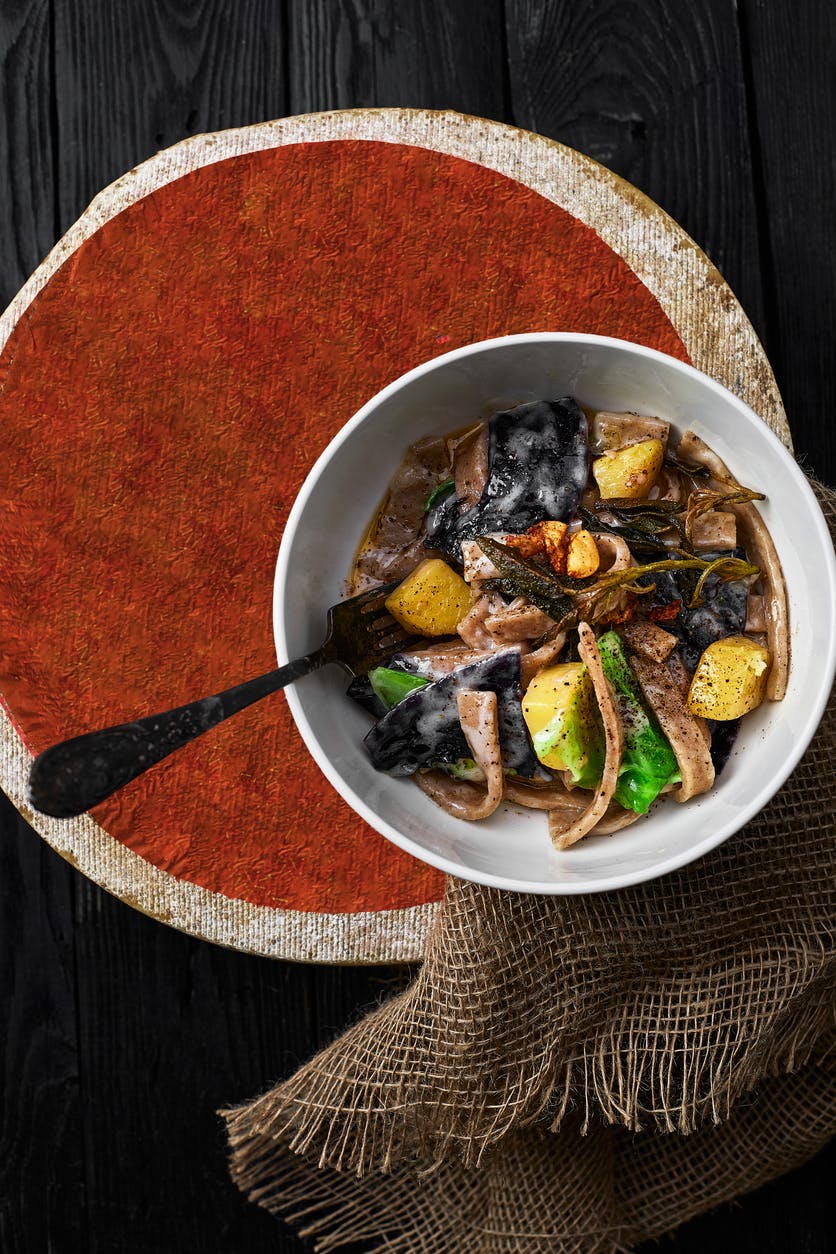 pasta pizzoccheri with chinese cabbage, potato on dark background. italian traditional dish