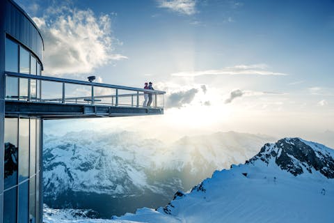 Kitzsteinhornin näköalatornissa kaksi henkilöä ihailee vuoristomaisemaa.