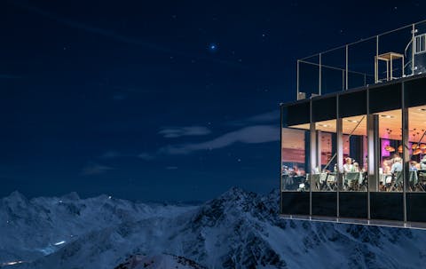 Söldenin Ice Q ravintolasta otettu kuva on kuvattu ulkoapäin. Ravintolan lasisista seinistä näkyy joukko ihmisiä syömässä ja maisemana on tähtitaivas vuoristossa.