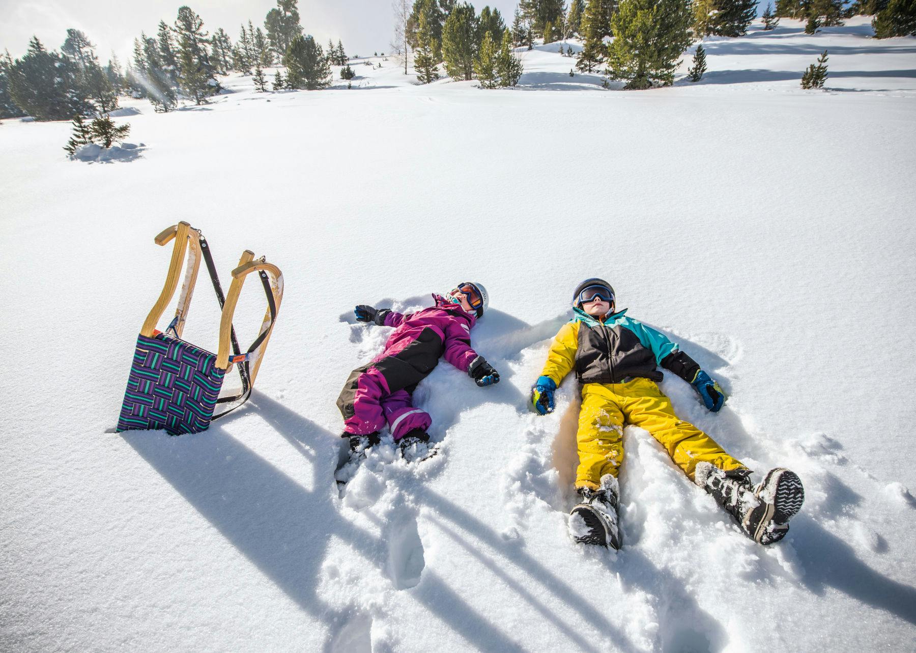 Lapset makaamassa lumessa ja kelkka heidän vieressään.