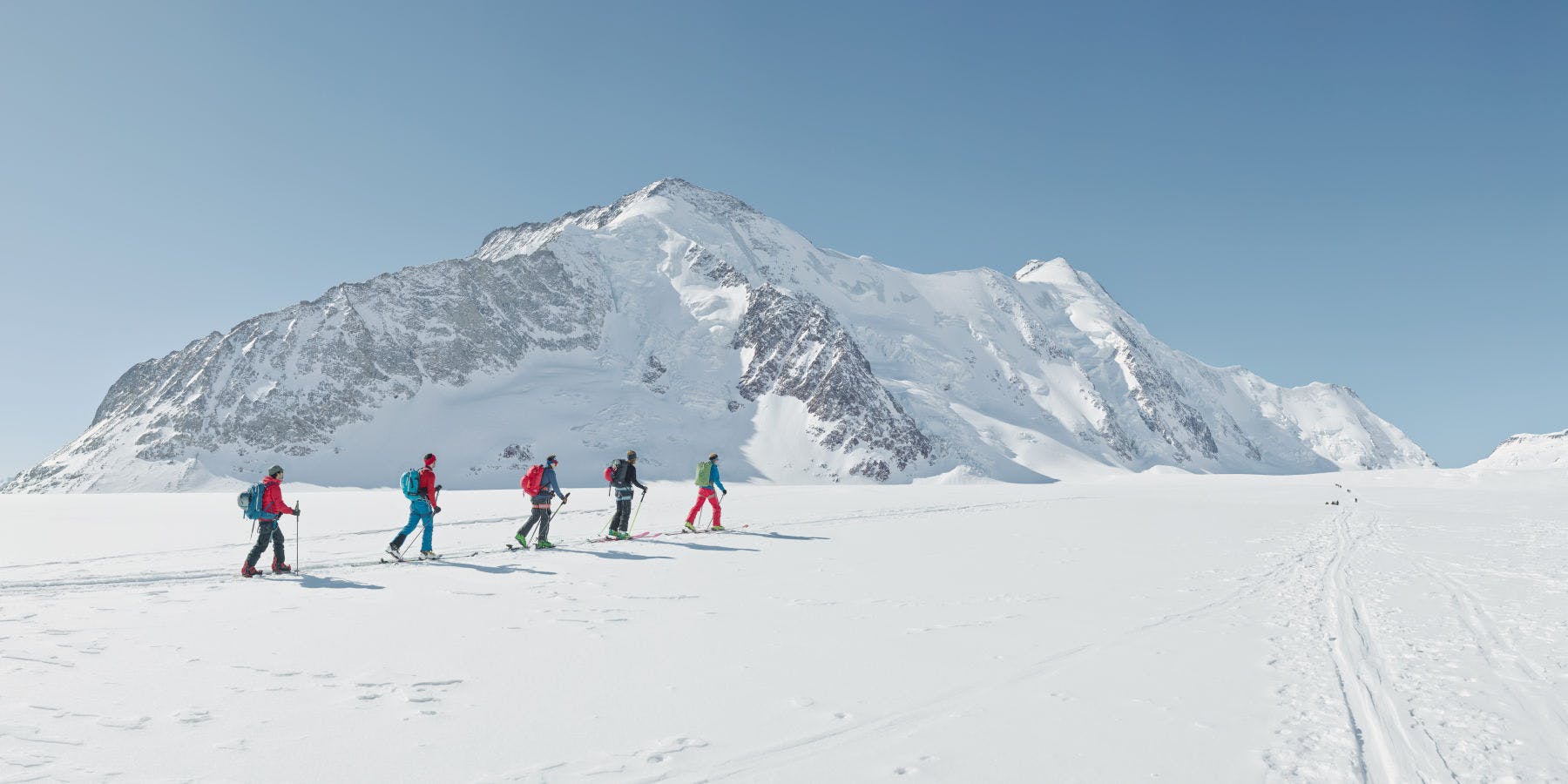 Murtomaahiihtäjät hiihtämässä vuoristossa. Luminen vuoristomaisema taustalla.