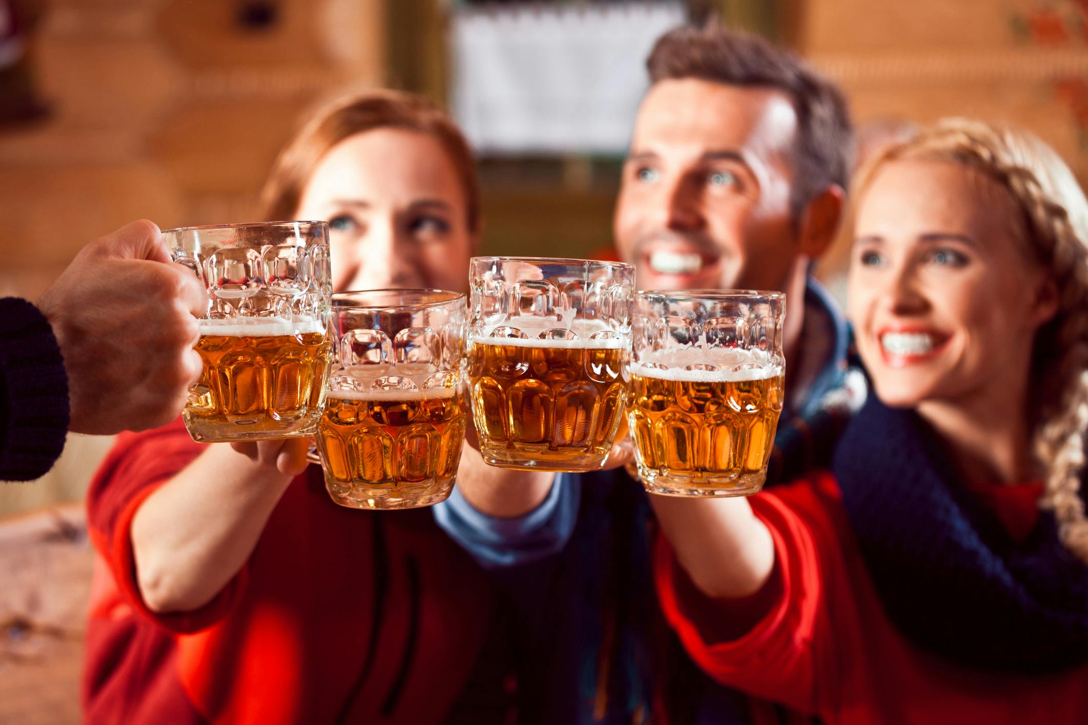 Neljä ihmistä kilistelee oluella. Kolmen kasvot hymyilevät ja neljännen henkilön käsi ainoastaan näkyy kuvassa.