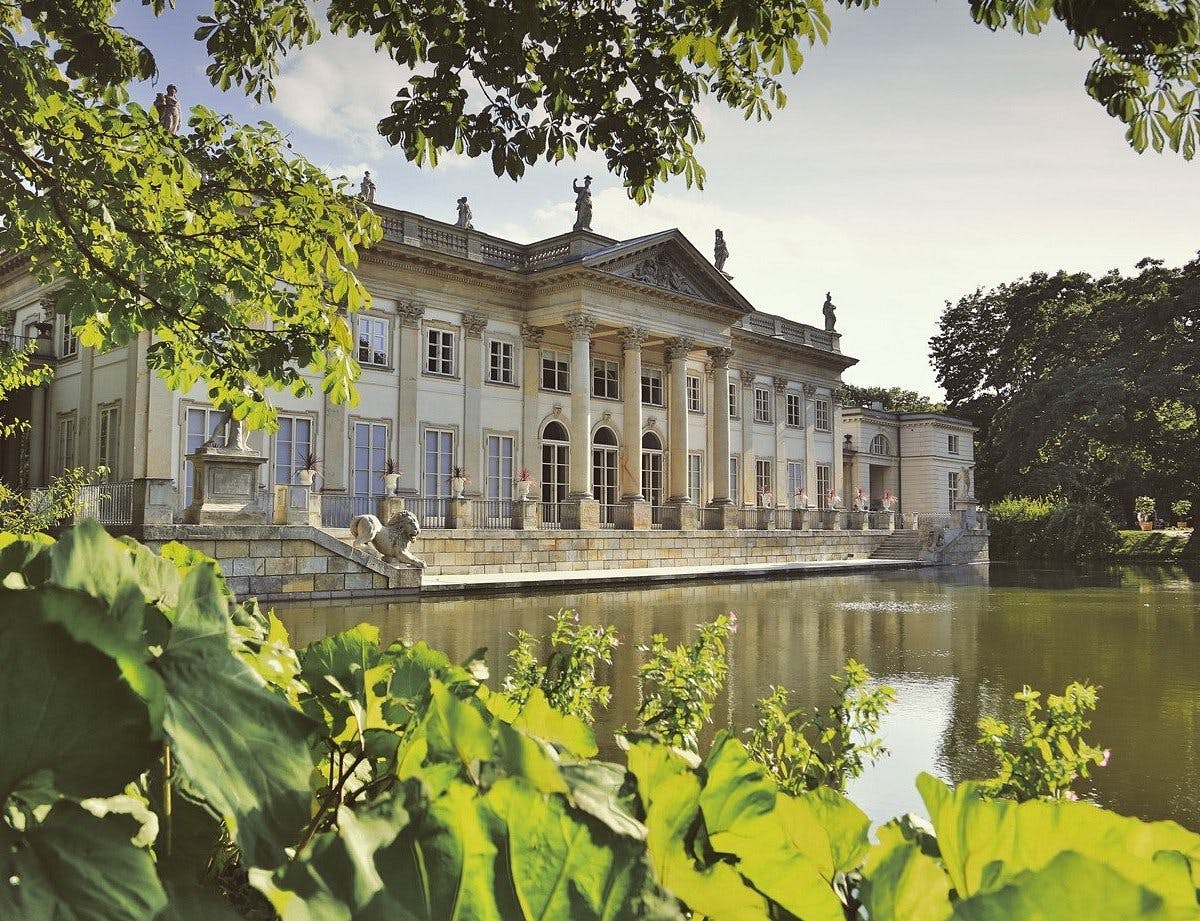 Kaunis klassinen palatsi veden äärellä vehreän luonnon ympäröimänä.