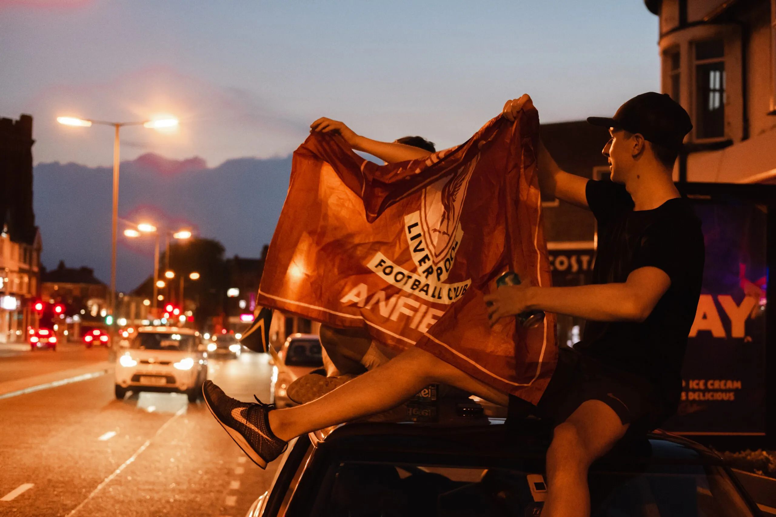 Liverpool FC fani istumassa auton katolla heiluttaen fanilippua