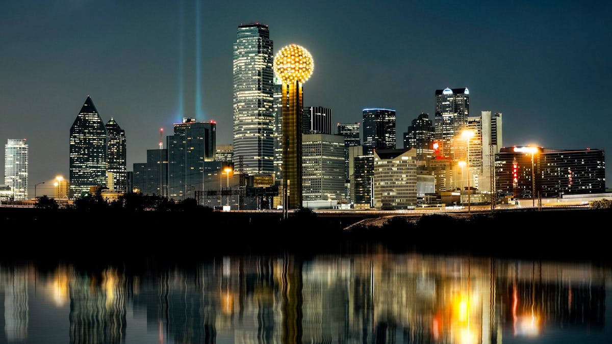 Maisemakuva Dallasista pimeällä. Korkeat rakennukset valaisevat kuvaa.