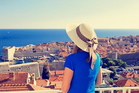 Hattupäinen nainen katselemassa Dubrovnikin kaupunkia yllään sininen t-paita