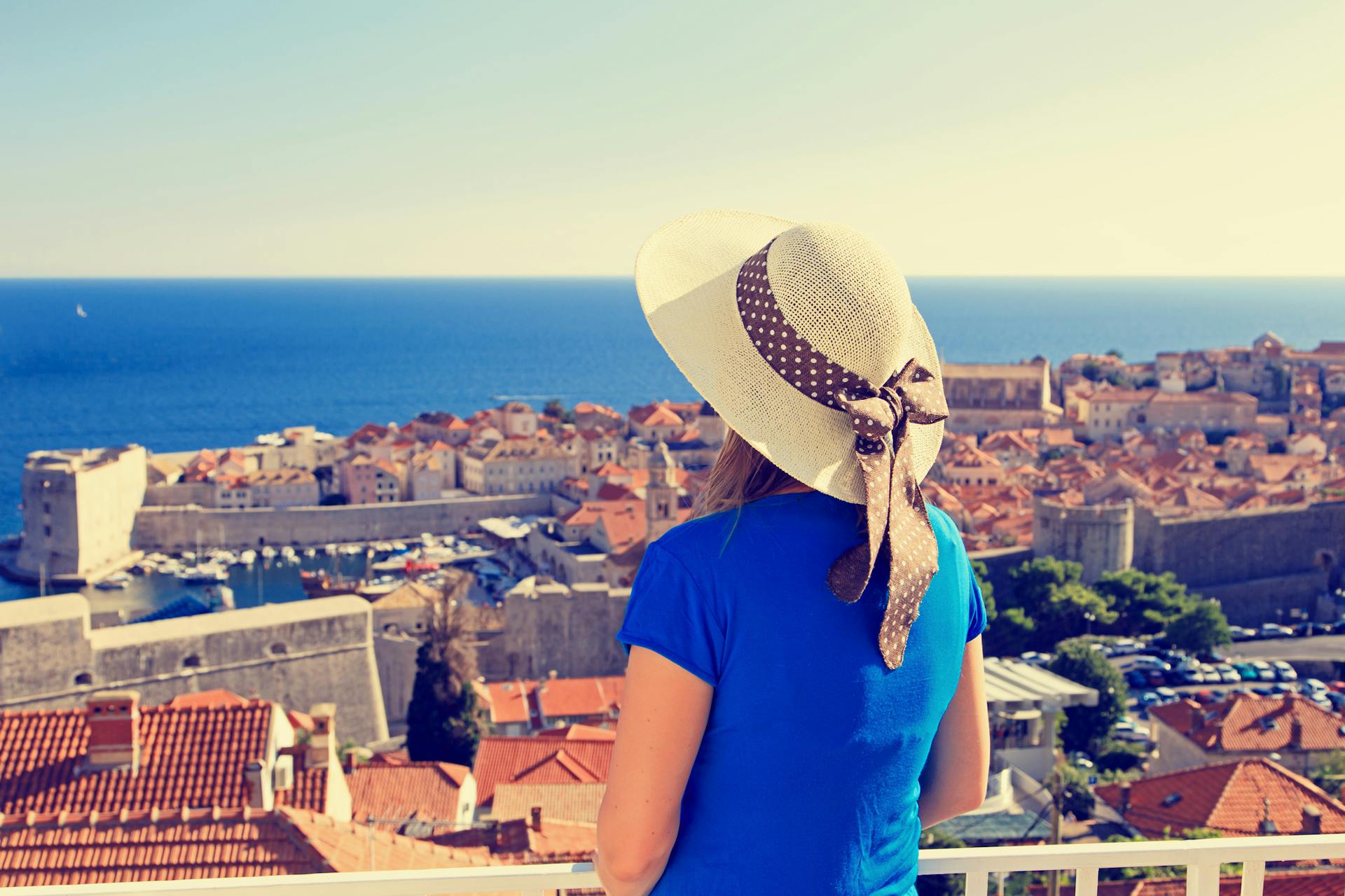 Hattupäinen nainen katselemassa Dubrovnikin kaupunkia yllään sininen t-paita