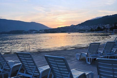 Näkymässä Dubrovnikin hiekkaranta, jossa on valkoisia aurinkotuoleja auringonlaskunaikaan