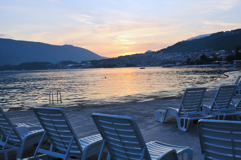 Näkymässä Dubrovnikin hiekkaranta, jossa on valkoisia aurinkotuoleja auringonlaskunaikaan