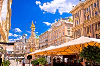 Näkymässä katunäkymää Wienistä, jonka edustalla ravintoloiden terasseja aurinkovarjoilla