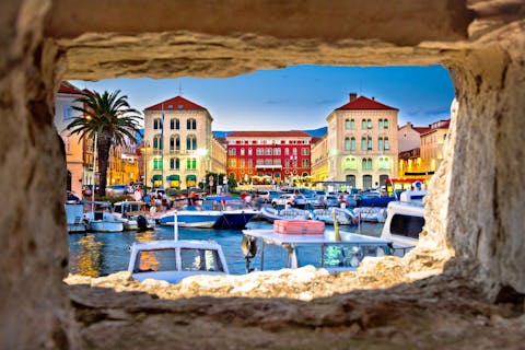 Näkymä kuvattu kivisen muurin sisältä, josta näkymä kohti Splitin värikkäitä rakennuksia ja satamaa, jossa on useita veneitä