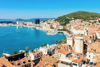 Maisemanäkymää Split kaupungista turkoosin meren edustalla. Näkymässä paljon rakennuksia sekä taustalla vihreä vuoristo